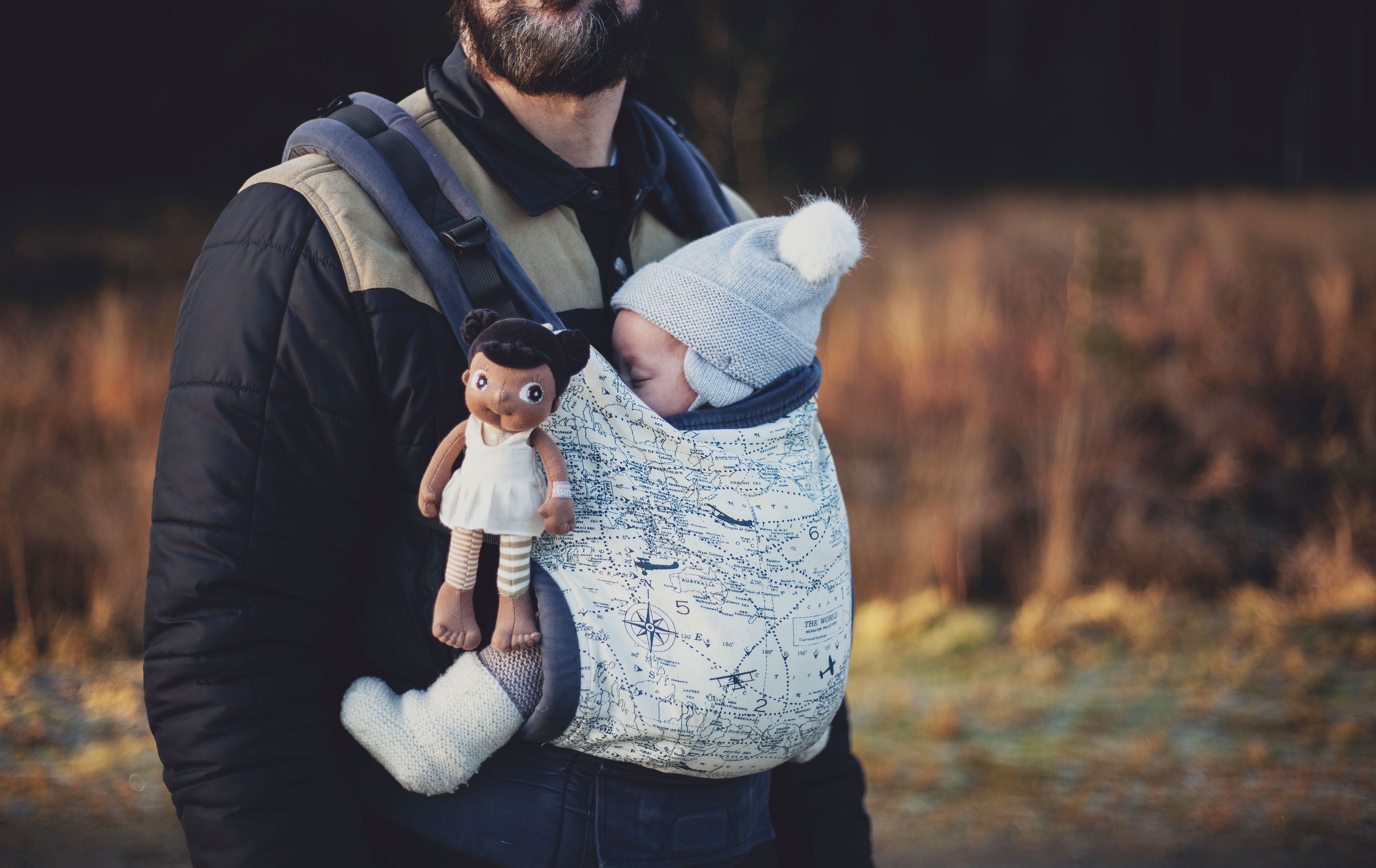 Die Rubens EcoBuds Mini-Puppe Flora steckt in einer Babytrage neben einem Baby