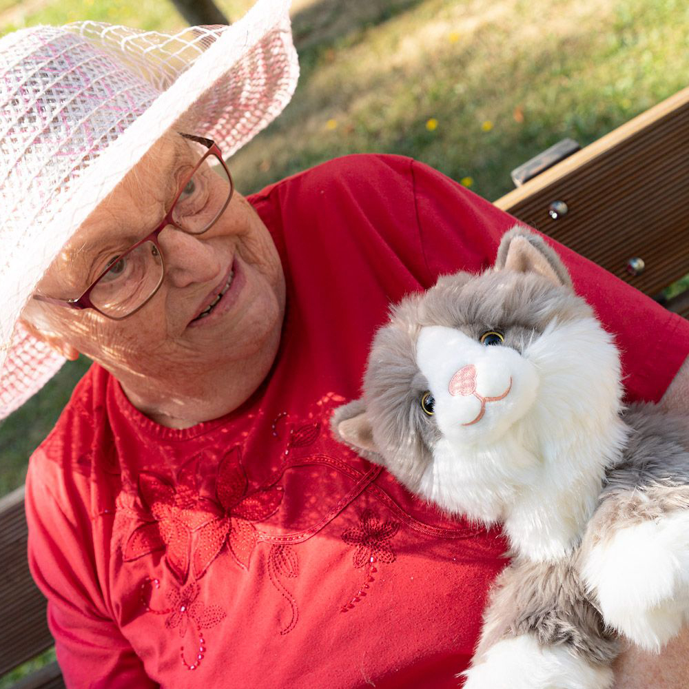 Senior lady with the Joyk empathy doll Billy in her arms on a park bench