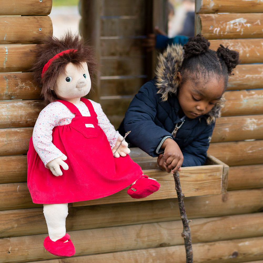 The Joyk empathy doll Ingrid sitting at the window of a playhouse next to a child