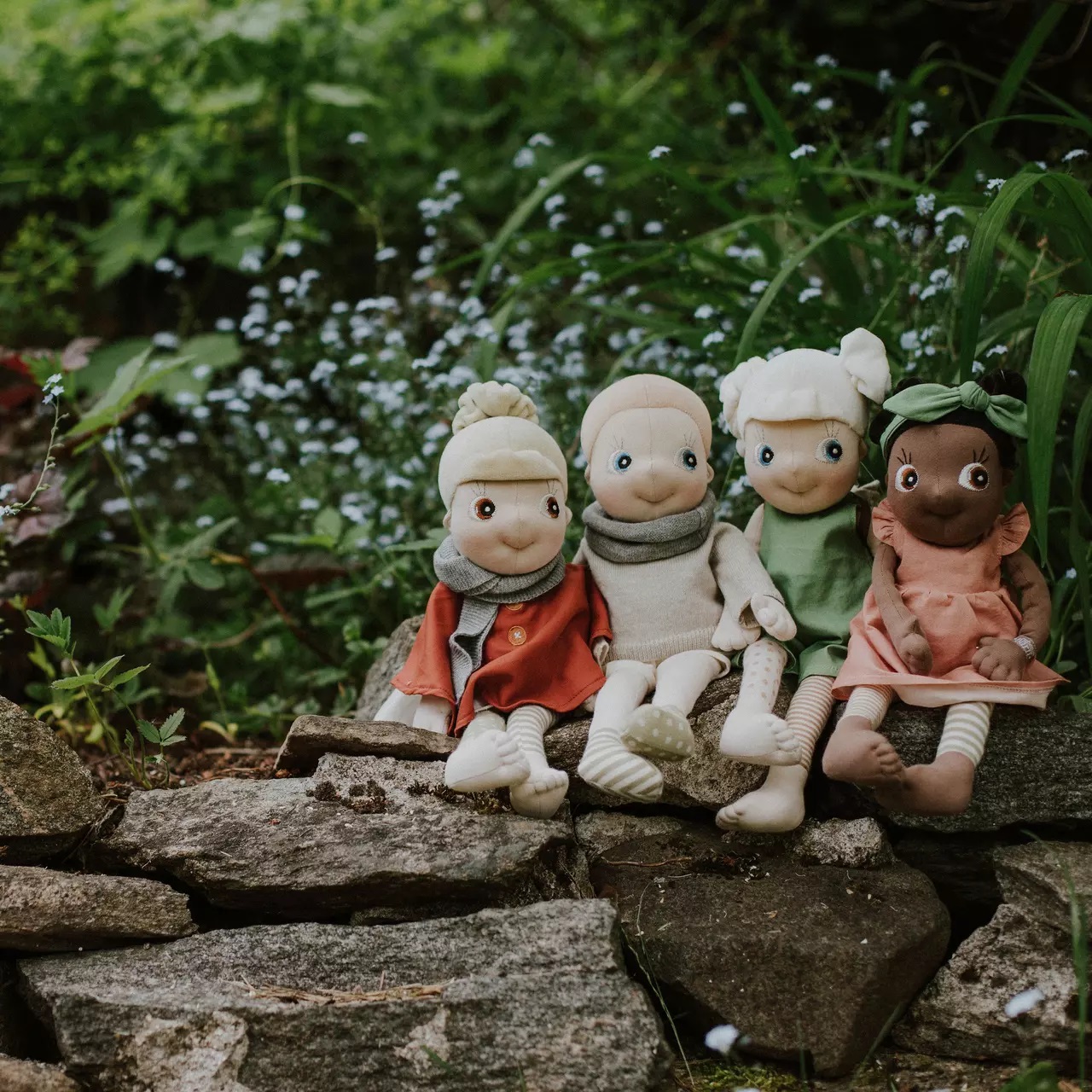 Vier Rubens EcoBuds Puppen in Saison-Outfits sitzen auf einer Gartenmauer