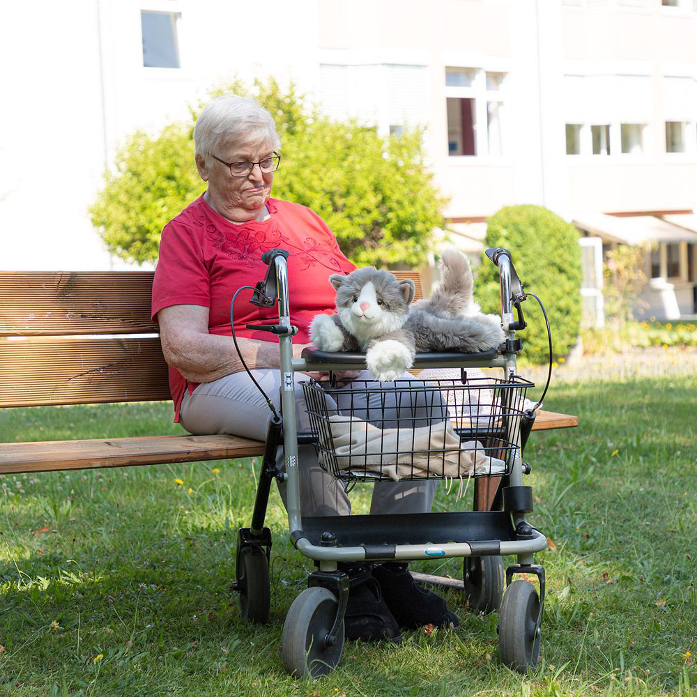 The Joyk empathy doll Billy lying on a rollator next to a senior lady in the garden