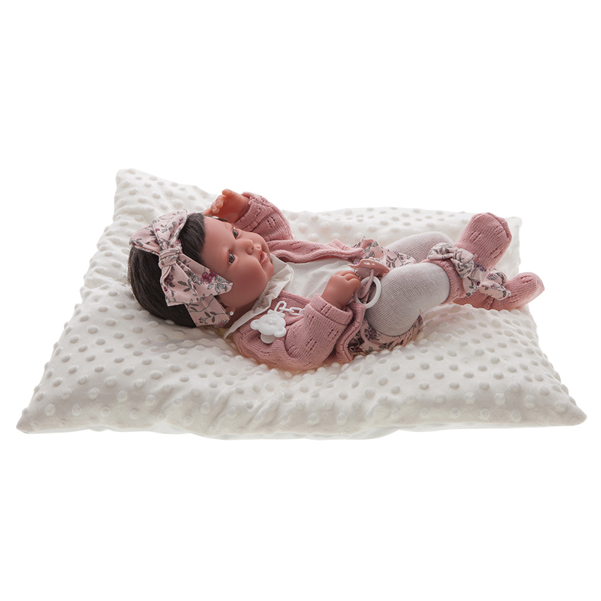 Antonio Juan Babypuppe Pipa, realistische Puppe mit dunklem Haar im rosa Blumenoutfit mit Schleifen-Stirnband, liegend auf weißem Kissen
