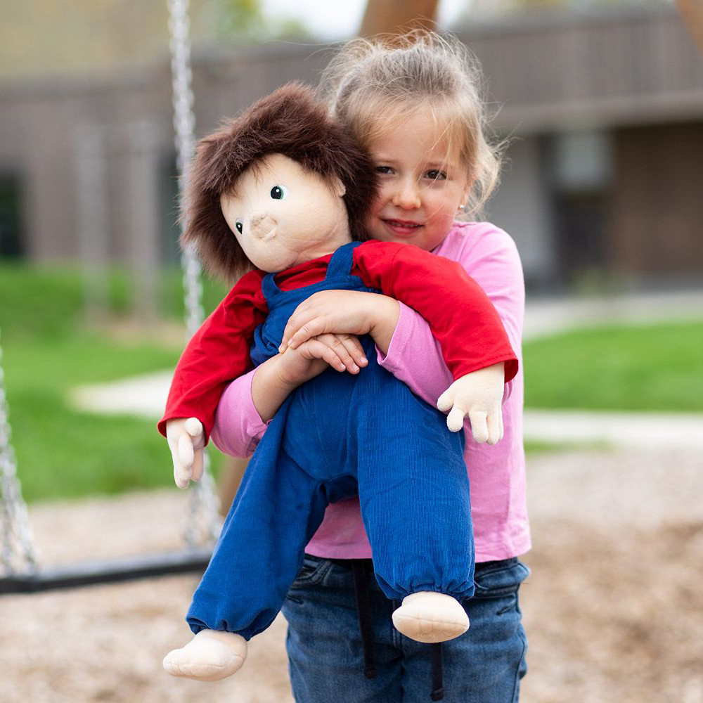 Child carrying the Joyk empathy doll Johan on the playground