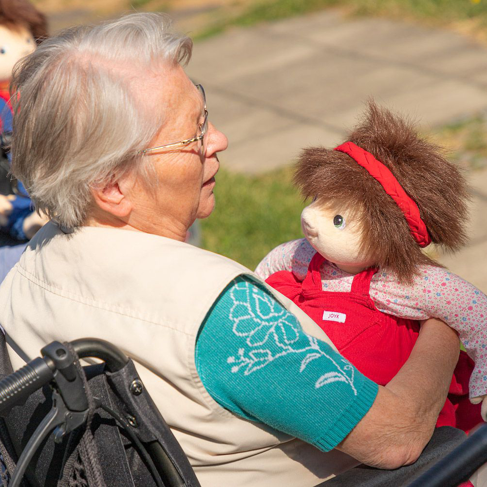 Senior lady holding the Joyk empathy doll Ingrid in her arms in the garden