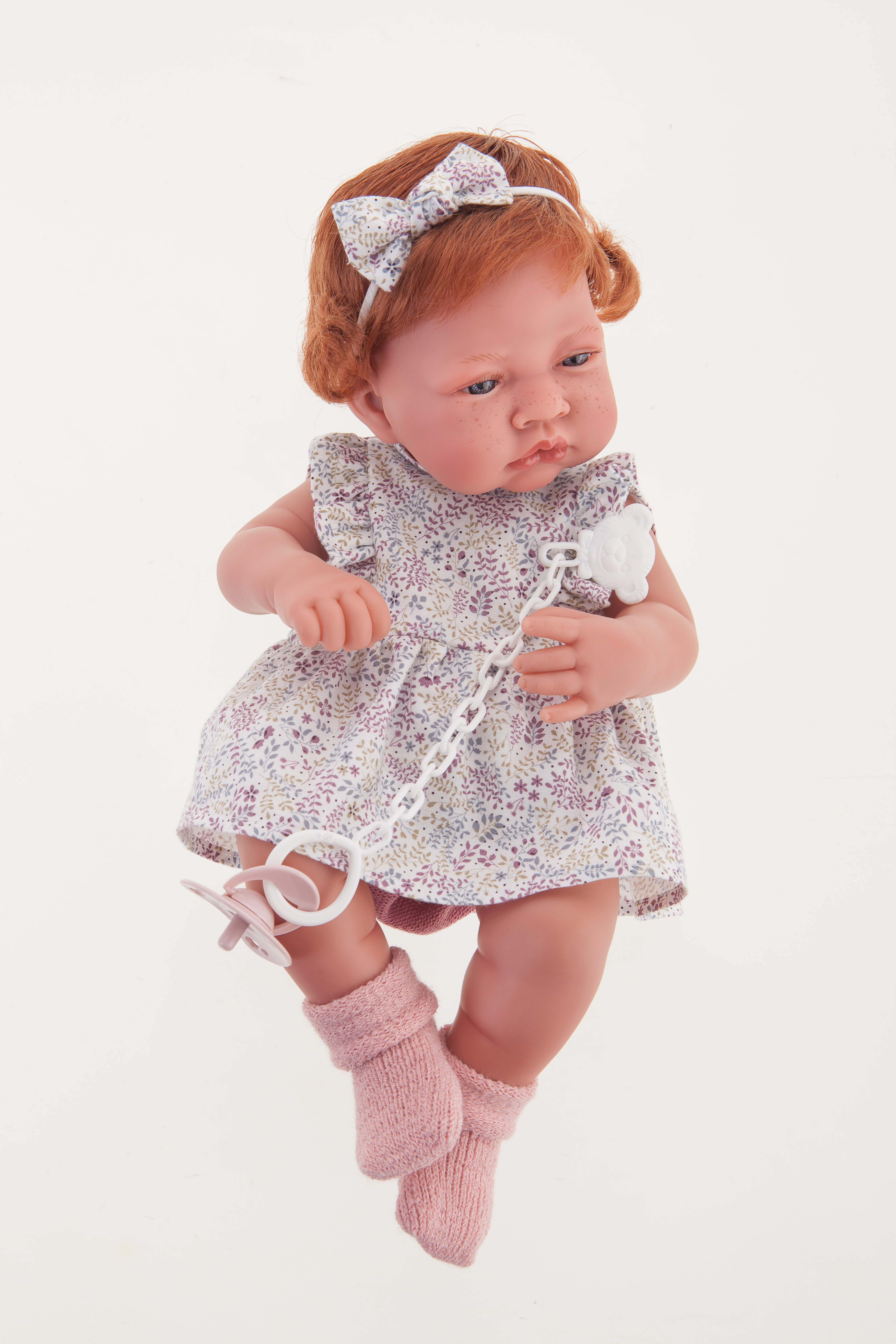 Antonio Juan Babypuppe New Born, realistische Puppe mit rotem Haar, Blumenkleid, Haarschleife und Schnullerkette, Frontalansicht