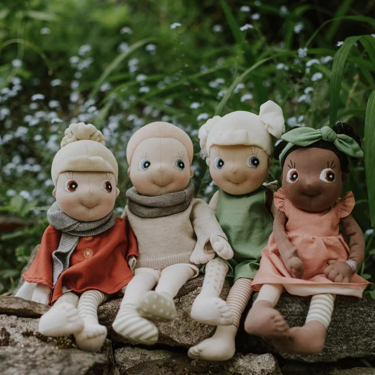 Vier Rubens EcoBuds Puppen in Saison-Outfits auf einer Steinmauer, Herbst in Rostrot