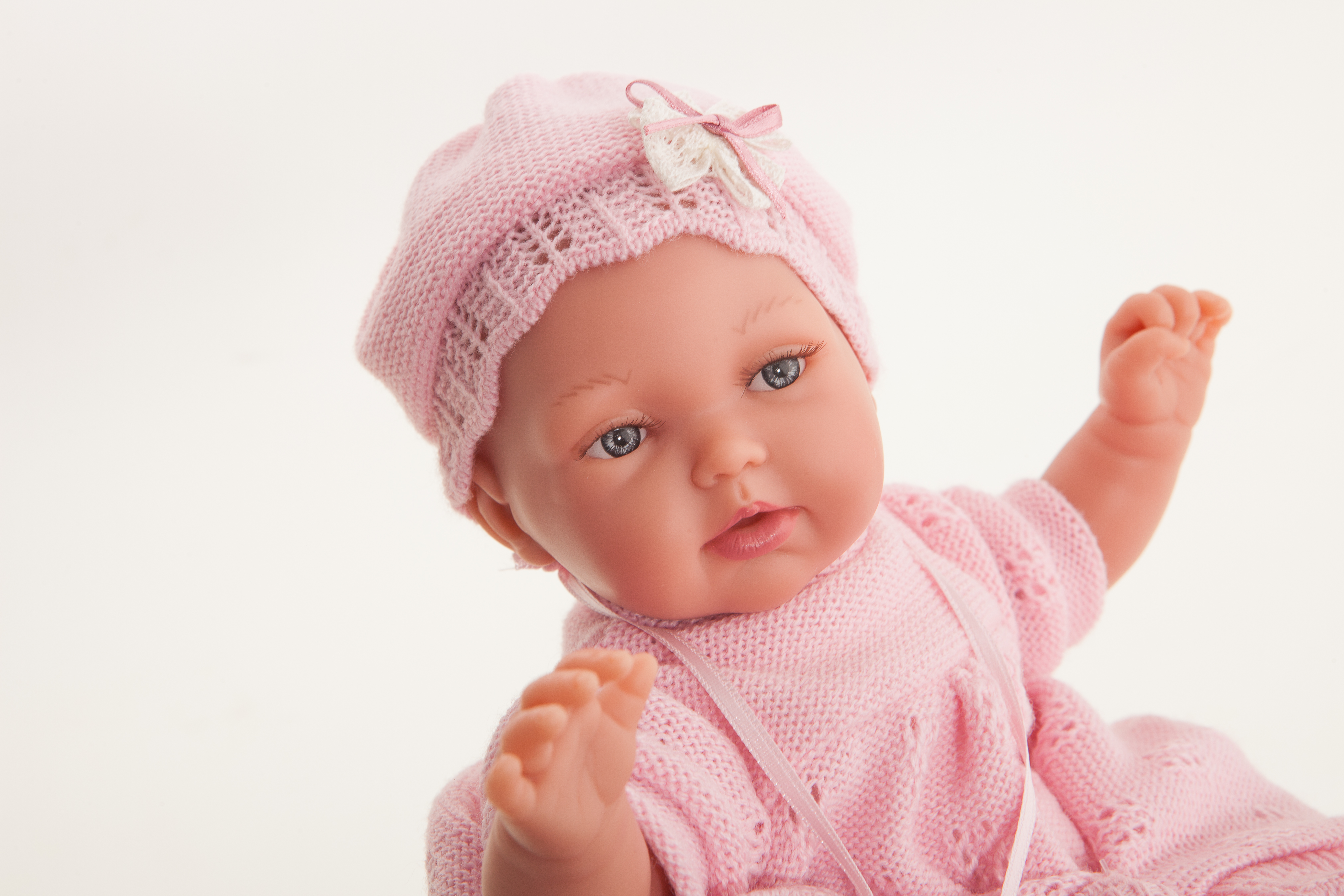Antonio Juan baby doll Peke, close-up of the face with blue eyes and a pink crocheted bonnet with bow