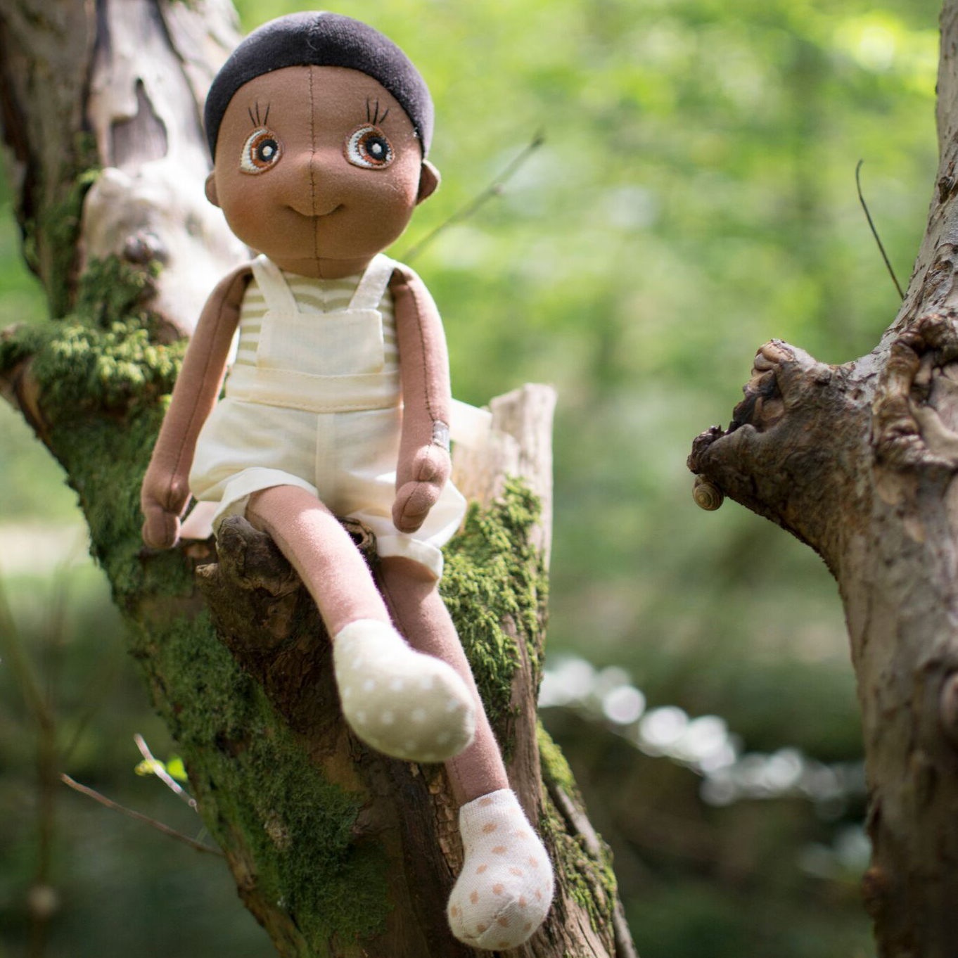 Die Rubens EcoBuds Puppe Fern sitzt auf einem bemoosten Ast im Wald