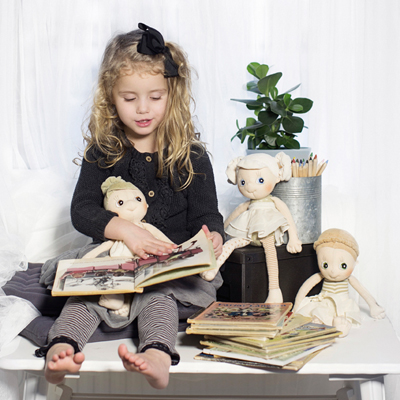 Child browsing picture books with the Rubens EcoBuds dolls, including Hazel