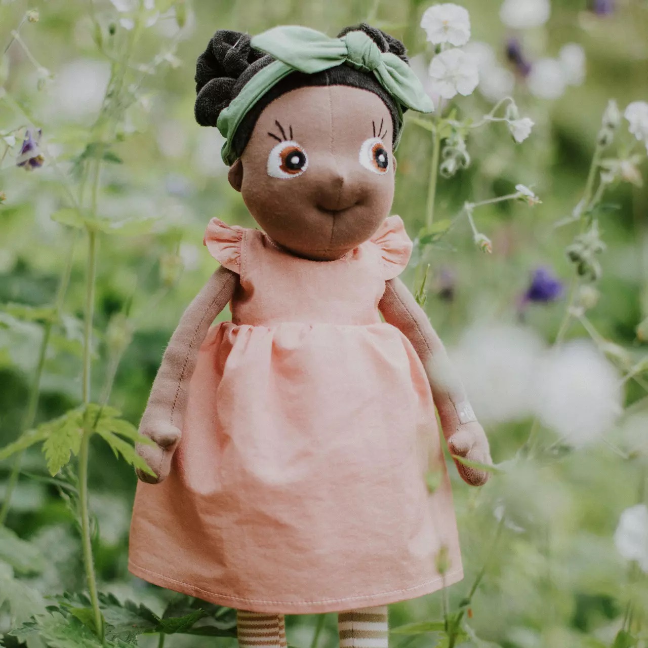 Rubens EcoBuds Puppe im rosa Sommerkleid mit grünem Haarband in einer Blumenwiese