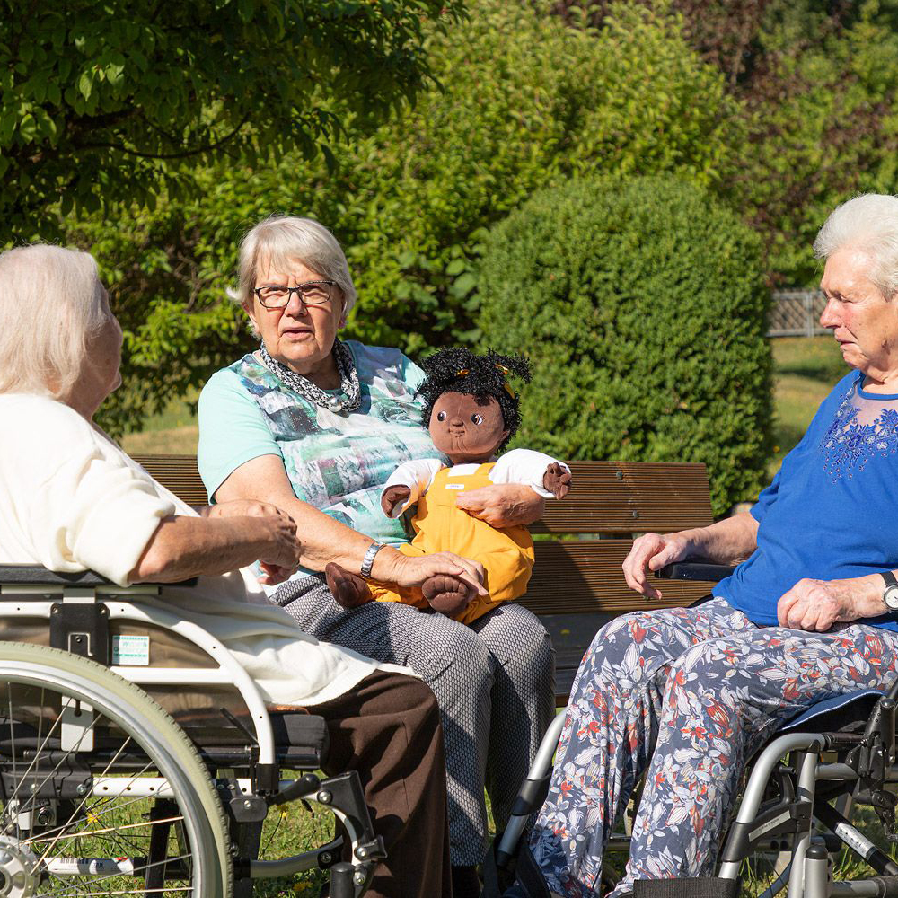 Group of senior ladies in the garden with the Joyk empathy doll Sofia on a lap
