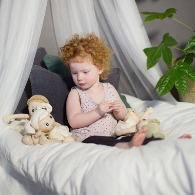 Child with the Rubens EcoBuds dolls, Hazel at their side, under the bed canopy