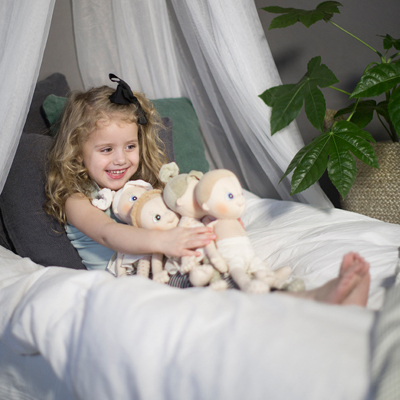 Child reaching for the Rubens EcoBuds dolls on the bed