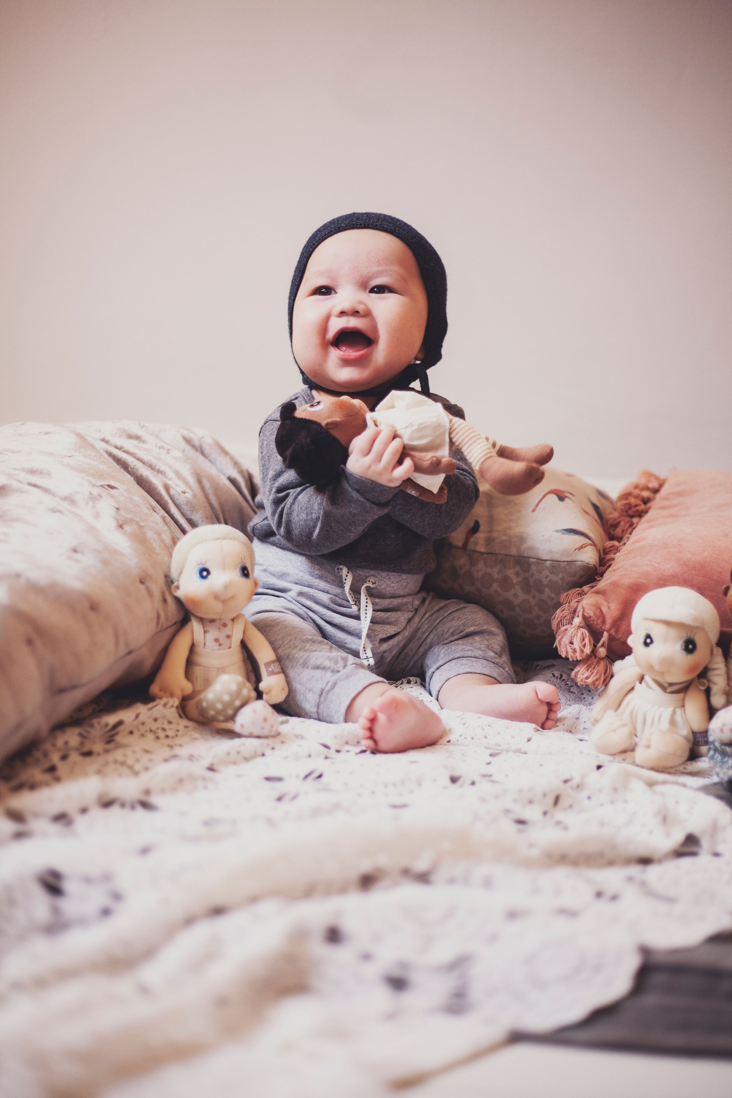 Lachendes Baby mit den Rubens EcoBuds Mini-Puppen auf dem Bett