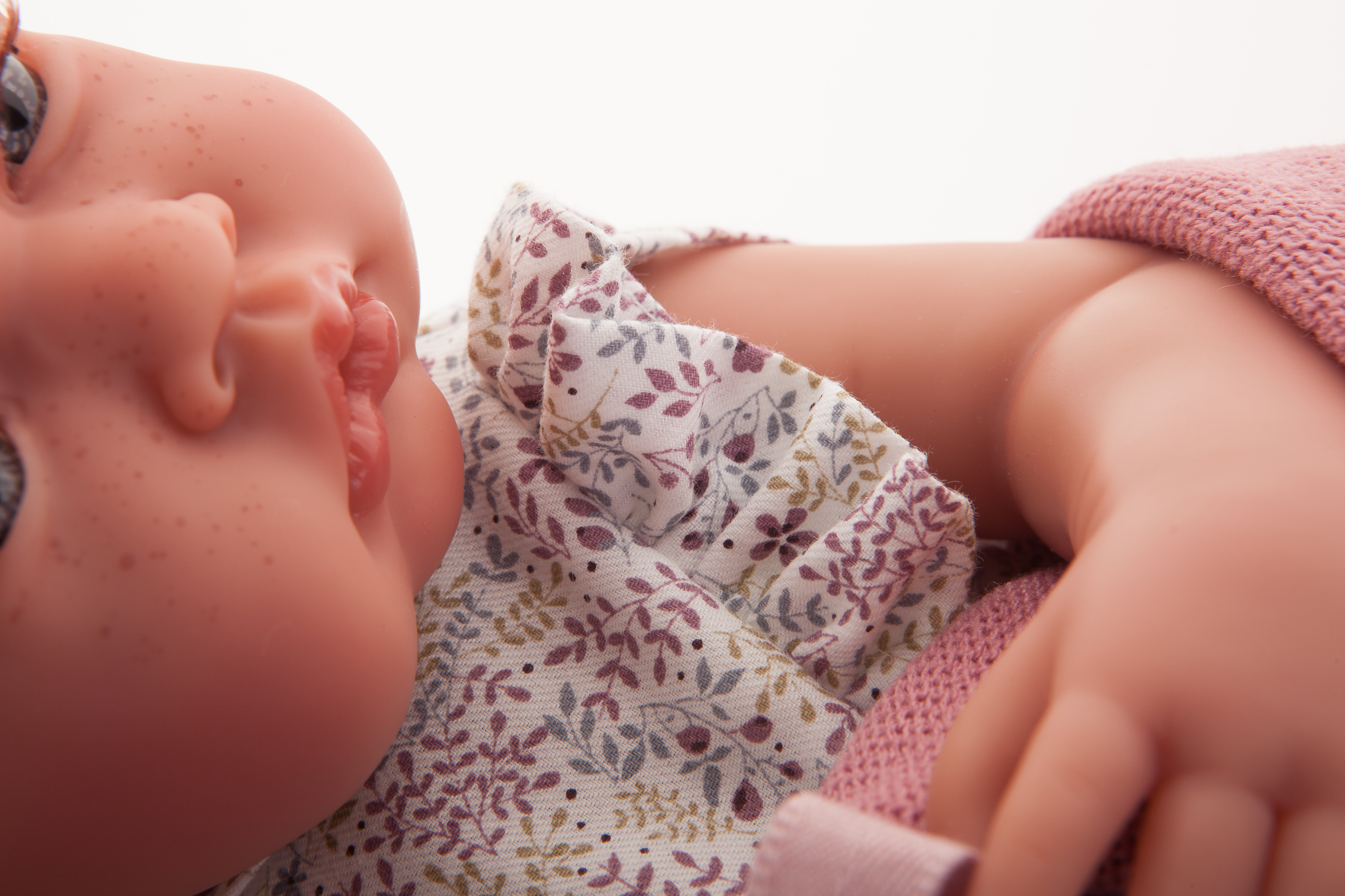Antonio Juan Babypuppe New Born, Nahaufnahme des seitlich gedrehten Gesichts mit Blumenkleid und altrosa Strickärmel