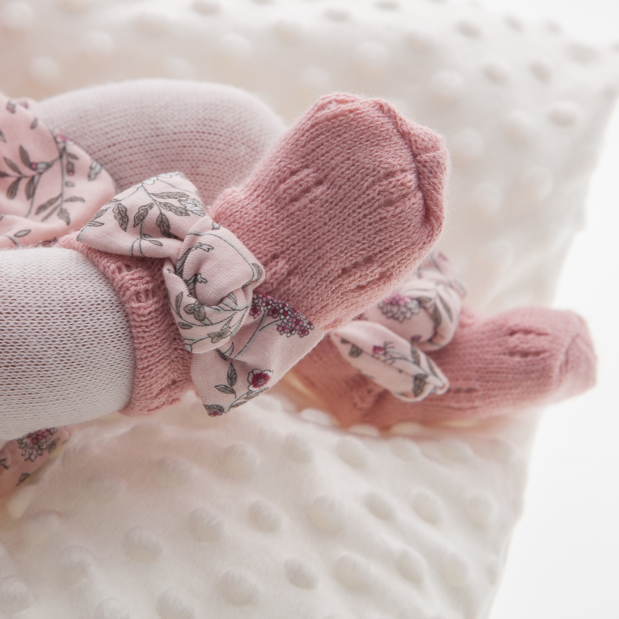 Antonio Juan baby doll Pipa, detail shot of the feet with floral bows and pink knit booties on a white pillow